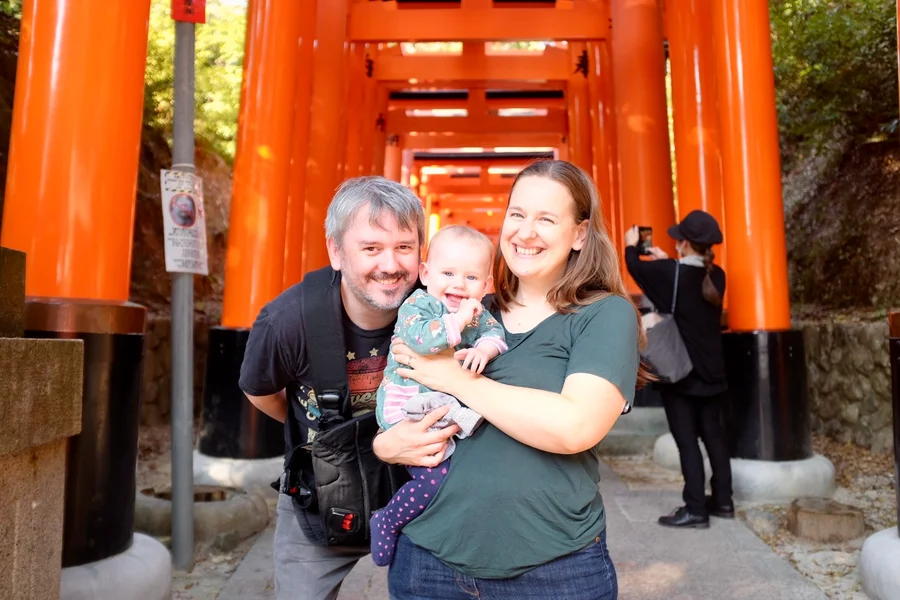 Family with baby smiling in front of the torii gate tunnel at Fushimi Inari shrine in Kyoto
