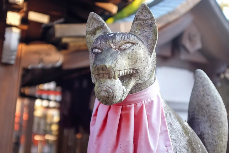 Close-up of a weathered stone kitsune fox guardian statue wearing a pink bib at Fushimi Inari shrine